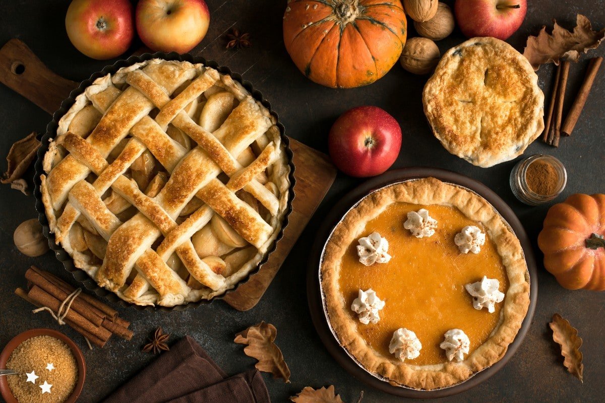 Three pies on a table surrounded by pumpkins and apples.