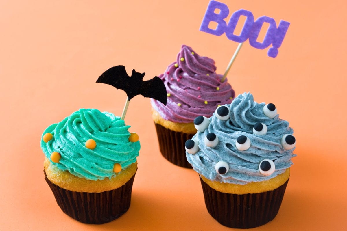 Three Halloween cupcakes on an orange background.